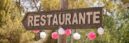 A rustic wooden restaurant sign in Spain, adorned with festive pink and white decorations amidst a natural outdoor setting.